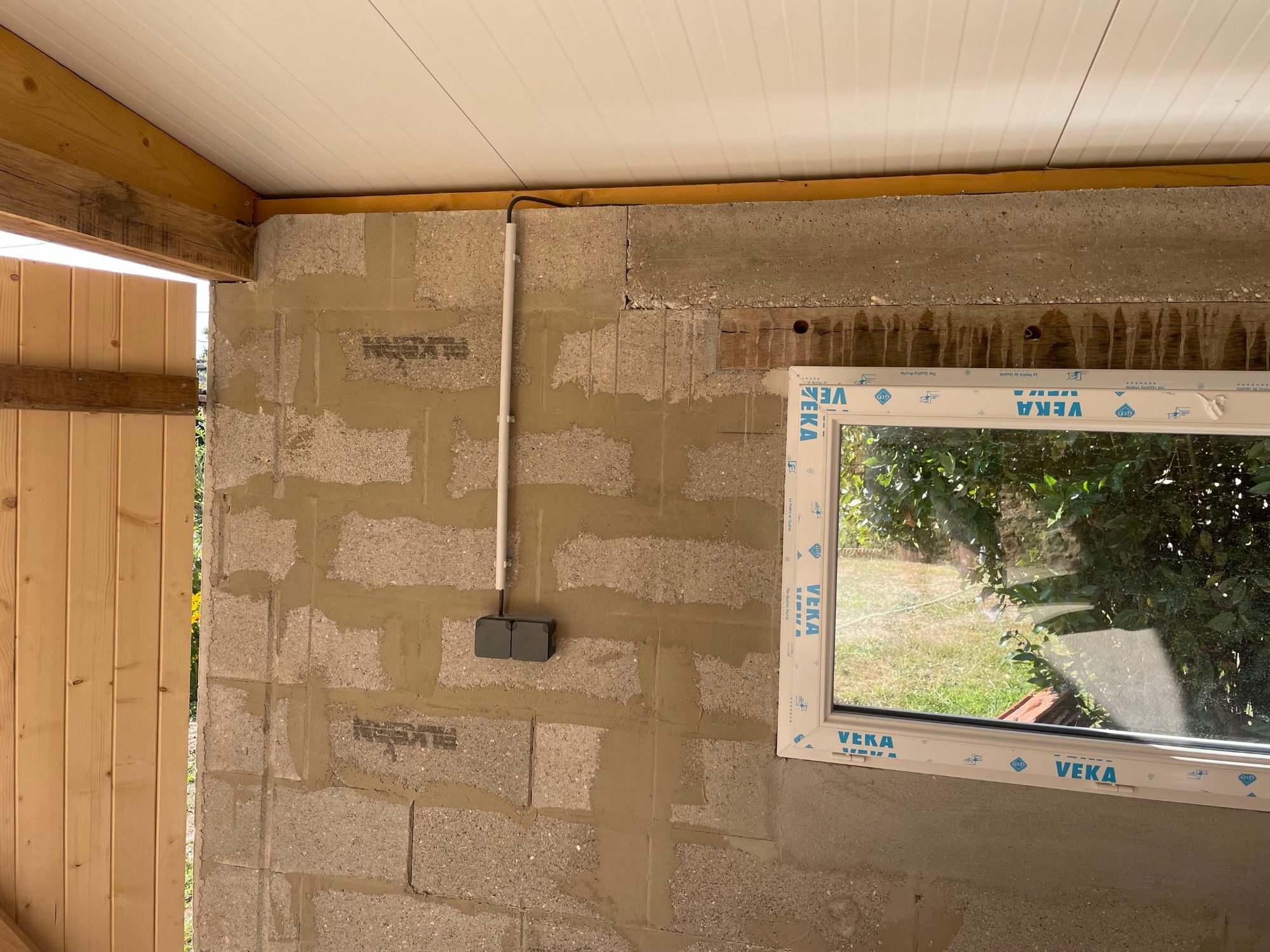 Prise double étanche posée sur mur en parpaings enduits avec conduit apparent – intérieur garage
